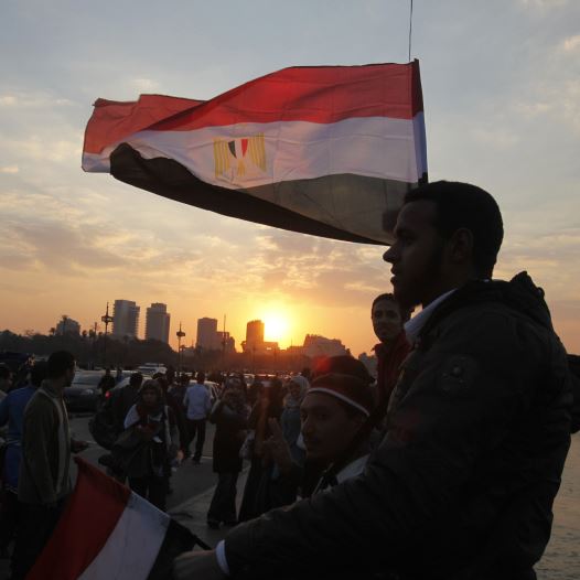 People stand on a bridge overlooking the river Nile as many Egyptians walk on the streets with Egyptian flags in Cairo
