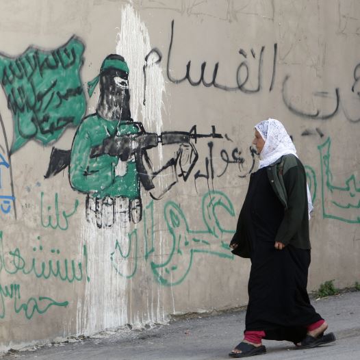 A Palestinian woman walks past a wall with graffiti depicting a gunman from the Al-Qassam brigades, the armed wing of the Hamas movement, in the West Bank village of Awarta. The graffiti reads ''All of us are martyrs.''