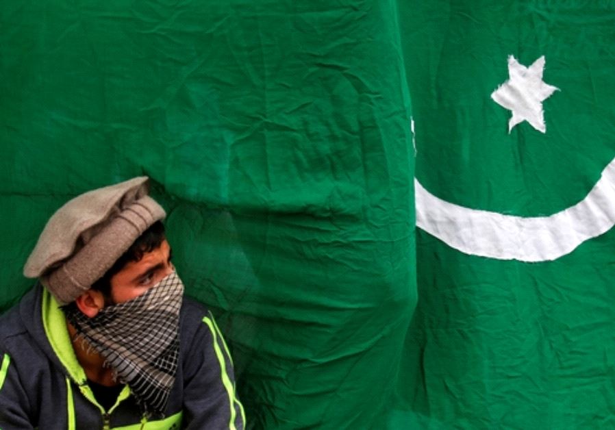 A masked protester sits next to a flag of Pakistan during an anti-Indian protest