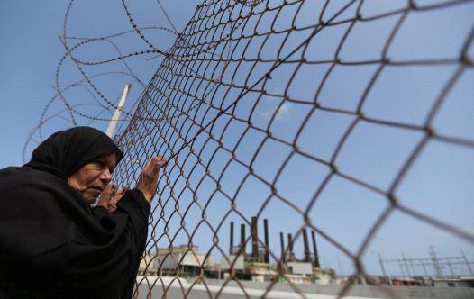 A Palestinian woman stands by a fence during a protest calling for an end to the power crisis, outside the power plant in the central Gaza Strip April 23, 2017.