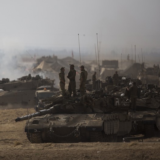 Israeli soldiers stand atop a tank at a staging area, near the border with the Gaza Strip