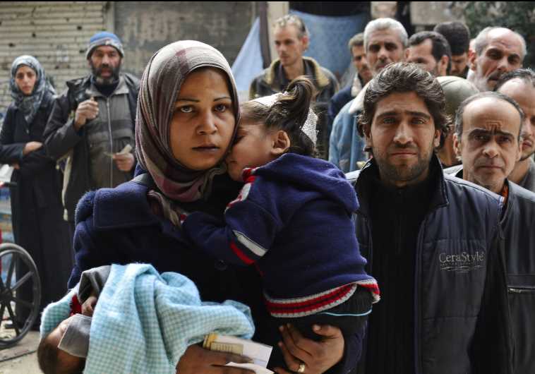 Residents queue up to receive humanitarian aid at the Palestinian refugee camp of Yarmouk, in Damascus.