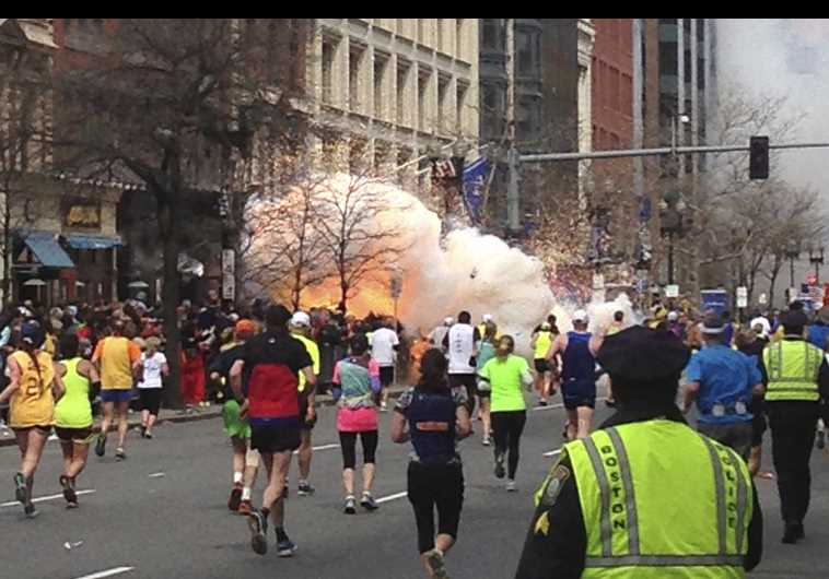 Runners continue to run toward the finish line of the Boston Marathon as an explosion erupts on April 15, 2013