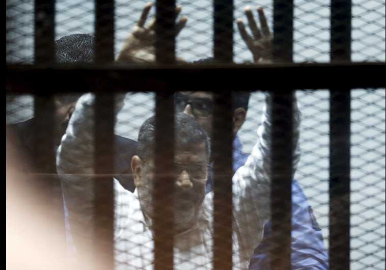 Ousted Egyptian President Mohamed Morsi gestures after his trial behind bars at a court in the outskirts of Cairo