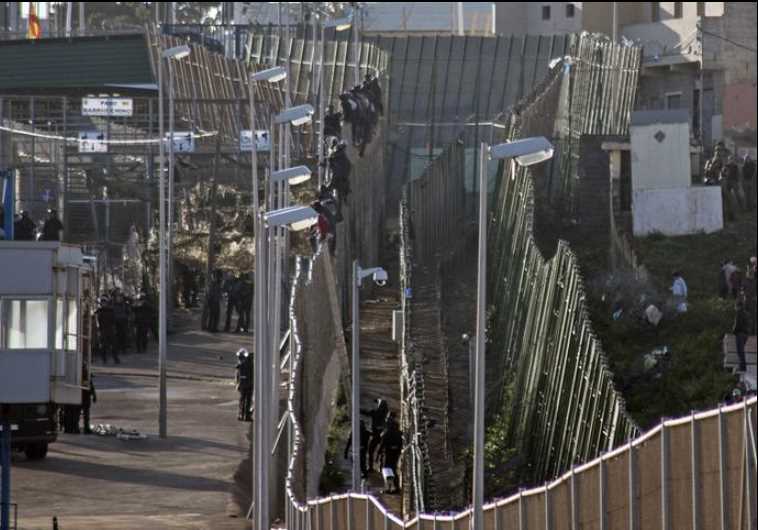 African migrants sit at the top of a border fence between Morocco and Spain's north African enclave.