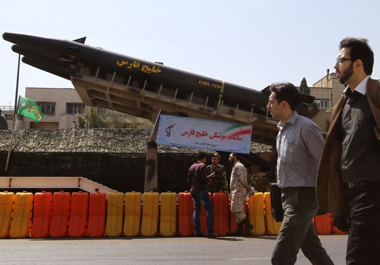 Iranian men walk past a long-range "Khalij Fars" anti-ship ballistic missile, displayed at a square in southern Tehran