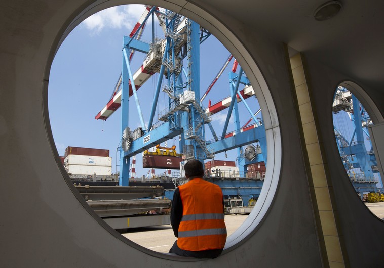 A worker sits as a crane unloads containers from a ship at the port of the northern city of Haifa