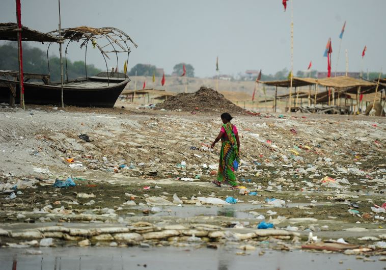 An Indian woman walks amogst plastic bags and garbage strewn on the banks of the River Ganges at Sangam