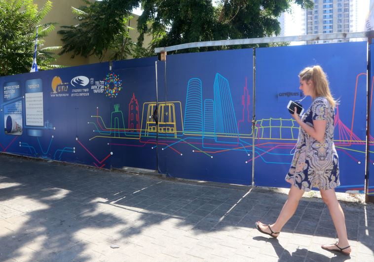 A woman walks in front of a sign advertising the Tel Aviv Light Rail 