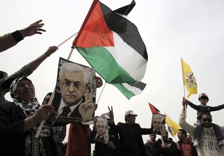 Palestinians hold flags and posters depicting PA Mahmoud Abbas during a rally in Bethlehem 