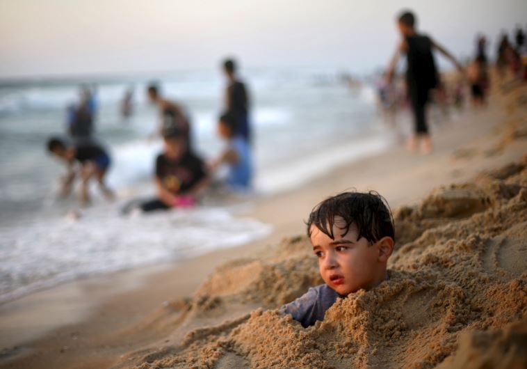 Palestinian boy buries himself in the sand at beach along the Mediterranean Sea in the northern Gaza Strip July 24, 2015. 