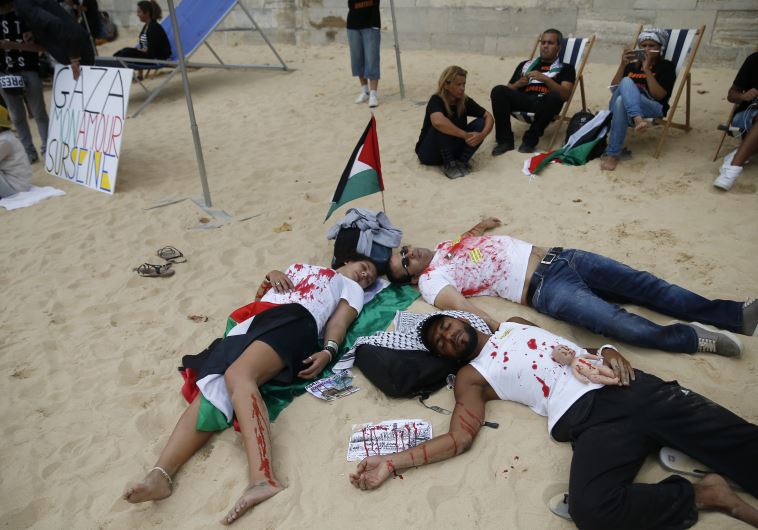 People covered in mock blood near a Palestinian flag and a placard which reads, "Gaza - My Love on Seine" stage their death on a artificial sand beach at "Paris Plages" to protest the "Tel Aviv on Seine" event, in Paris