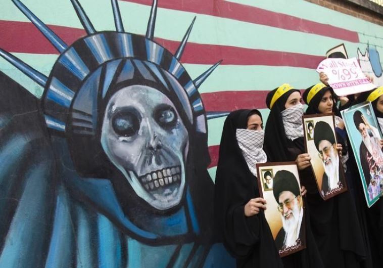 Iranian students hold pictures of Iran's Supreme Leader Ayatollah Ali Khamenei in front of an anti-US mural, painted on the wall of the former US Embassy in Tehran