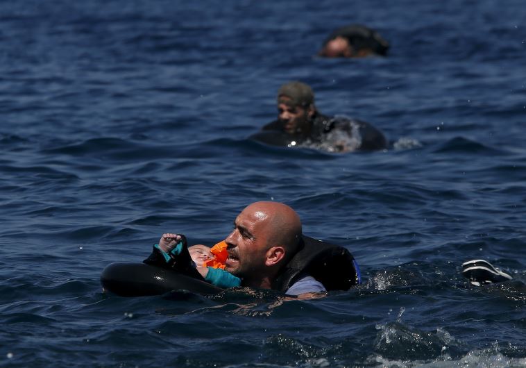A Syrian refugee holding a baby in a lifetube swims towards the shore after their dinghy deflated some 100m away before reaching the Greek island of Lesbos