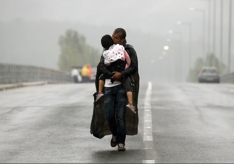 A Syrian refugee kisses his daughter as he walks through a rainstorm towards Greece's border with Macedonia, near the Greek village of Idomeni