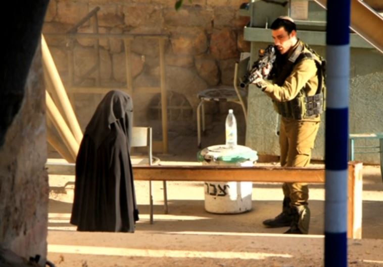 An IDF soldier aiming at Hadeel al-Hashlamun after she refused requests to put down her weapon and lunged at soldiers