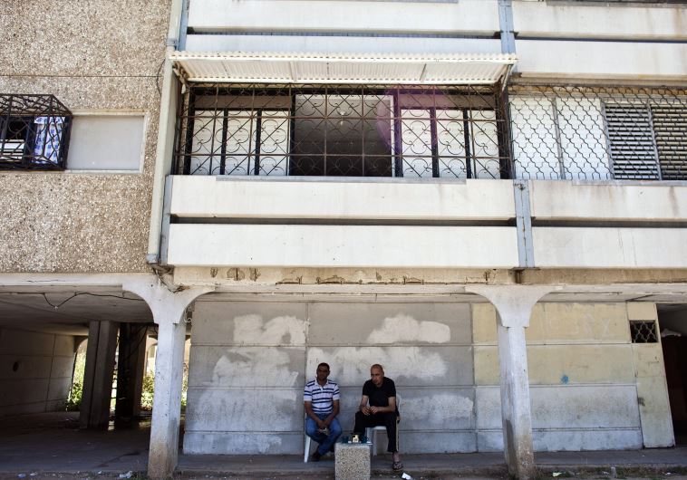 Residents sit with cups of coffee outside their apartment building in Lod