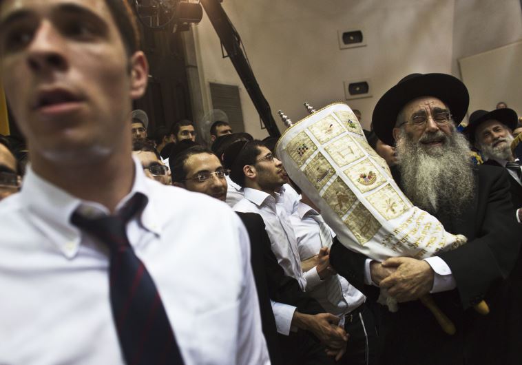 An Ultra-Orthodox Jewish Rabbi carries Torah scrolls as others dance during Simhat Torah celebrations in a synagogue in Bnei Brak