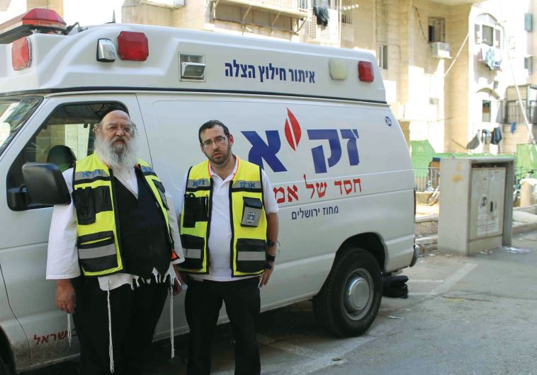 Zaka first responders Yossi Frankel (right) and Benzi Oring pose in front of one of the organization’s emergency vehicles