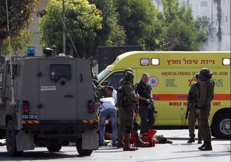 Israeli soldiers gather around the body of a Palestinian man who was shot dead after stabbing and wounding a soldier at the entrance to Hebron