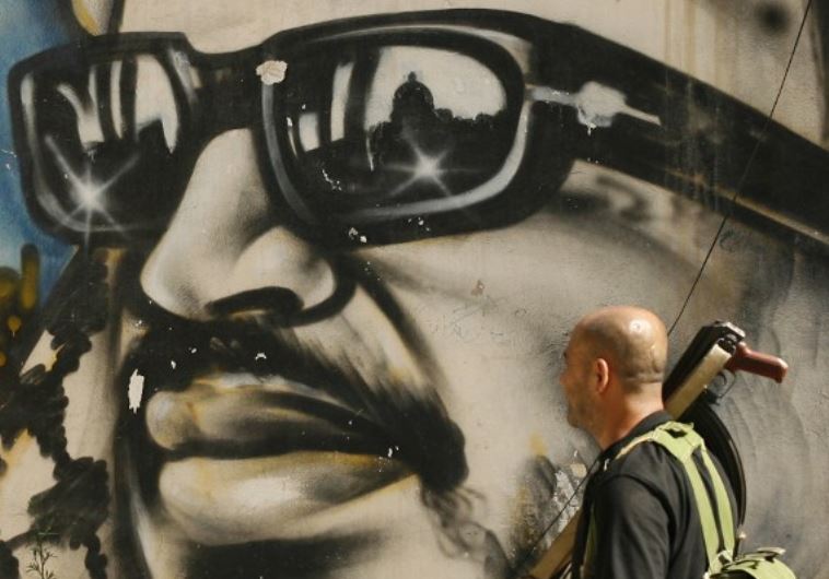 An armed man walks past a graffiti depicting late Palestinian leader Yasser Arafat in Lebanon's southern Palestinian refugee camp of Ain El-Helweh