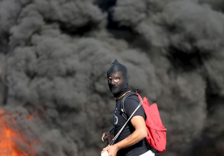 A Palestinian protester takes a position as smoke rises from a fire behind him during clashes with Israeli troops near the Jewish settlement of Beit El