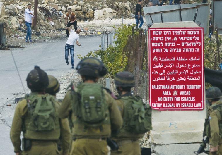 A Palestinian youth throws a stone during clashes with Israeli soldiers next to the scene of a stabbing attack near Hebron on October 26