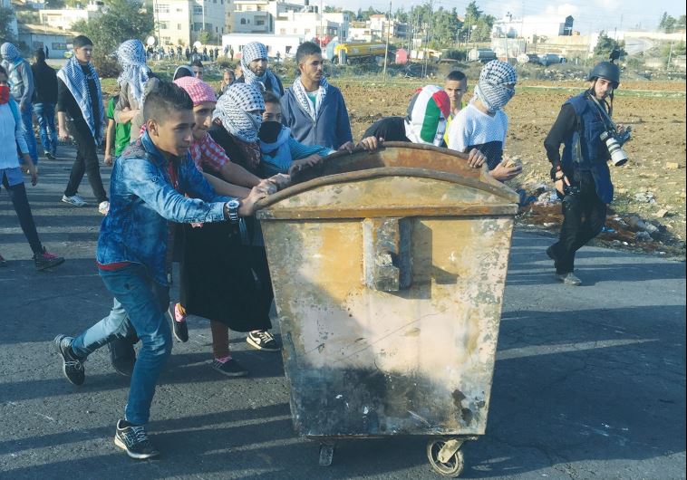 PALESTINIAN PROTESTERS push a dumpster toward the DCO checkpoint near Ramallah