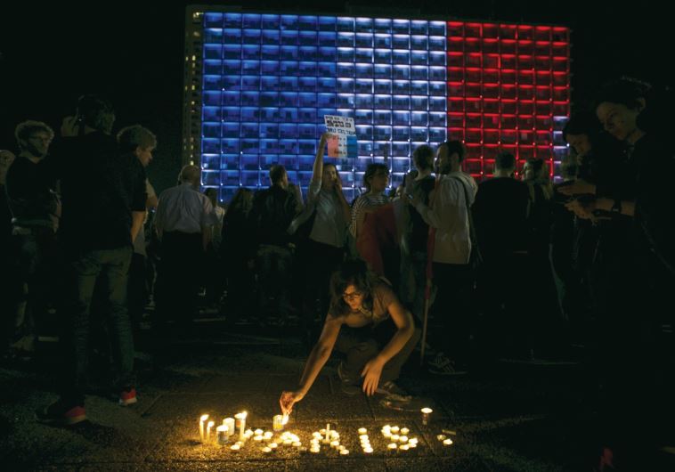 A woman lights candles during a ceremony honoring victims of the attacks in Paris, as the Tel Aviv municipality is lit up in the blue, white and red colors of the French flag, on November 14