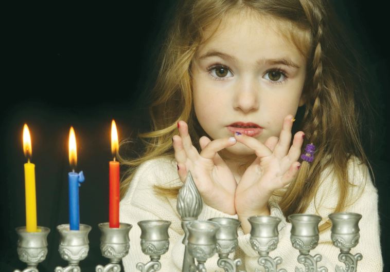 A young girl lights a hanukkia