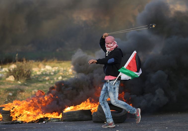 A Palestinian protester uses a sling to throw stones towards Israeli troops during clashes, near the Jewish settlement of Bet El, near the West Bank city of Ramallah November 29, 2015