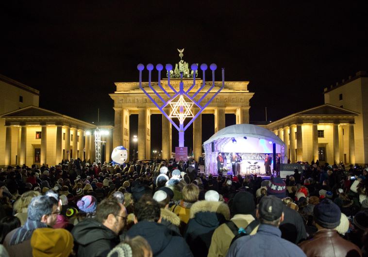 People stand in front of a giant eight- branched candelabrum Menorah in front of the Brandenburg Gate in Berlin on December 6, 2015 at the start of the holiday of the jewish religious festival of lights Hanukkah.
