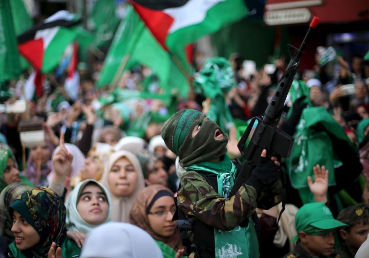 A masked Palestinian boy holds a toy gun as he takes part in a rally marking the 28th anniversary of Hamas' founding