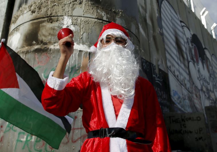 A Palestinian protester wearing Santa Claus costume stands in front of a section of the Israeli barrier during an anti-Israel protest in the West Bank city of Bethlehem December 18, 2015