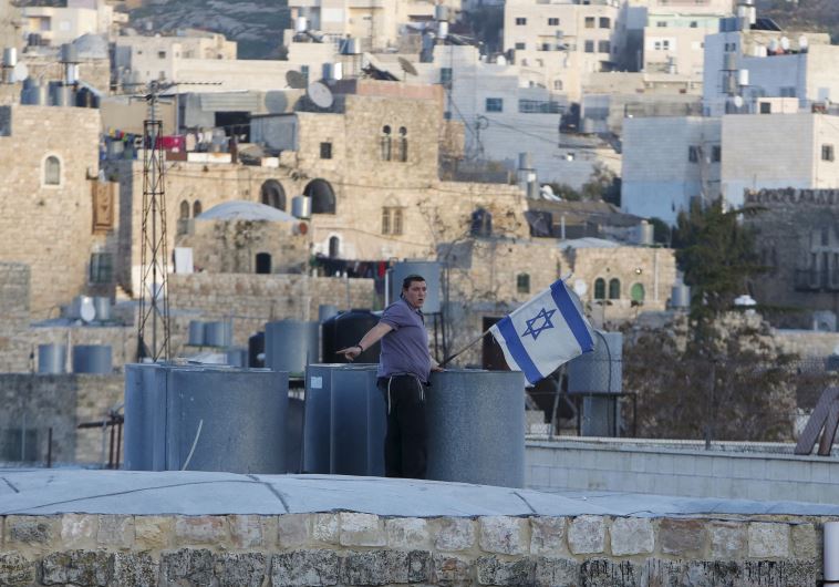 An Israeli settler puts up an Israeli flag over a house, which is disputed between Palestinians and Israelis, in Hebron