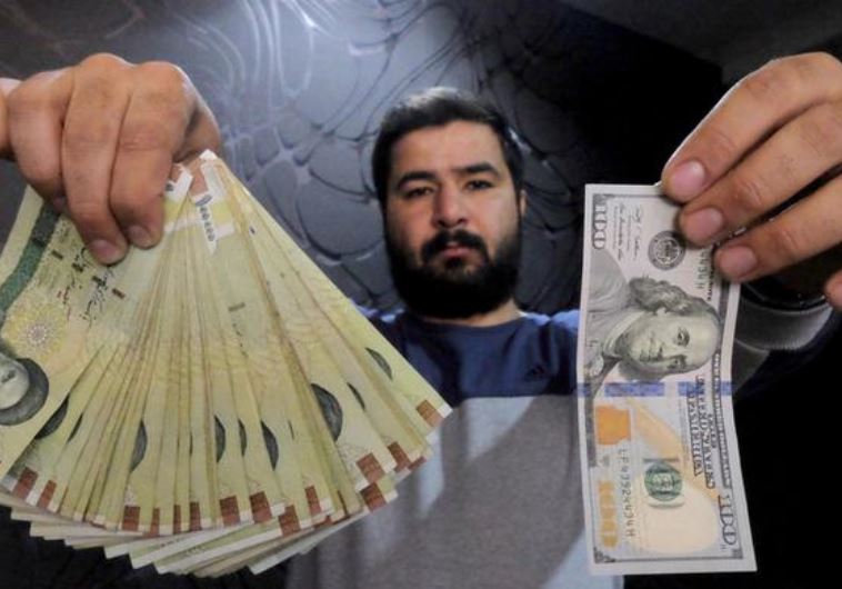 A money changer poses for the camera with a U.S dollar (R) and the amount being given when converting it into Iranian rials (L), at a currency exchange shop in Tehran's business district, Iran, January 20, 2016.