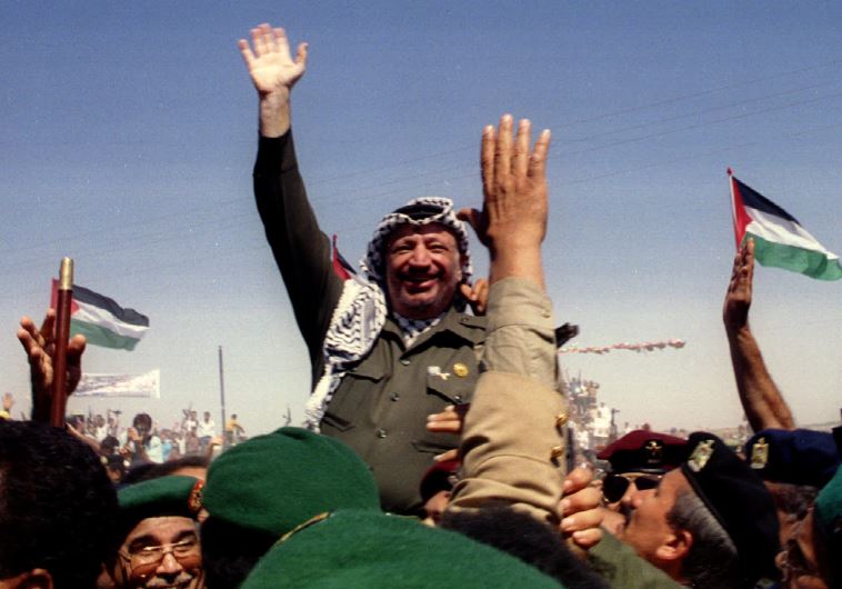 Palestine Liberation Organization chairman Yasser Arafat waves as he is briefly lifted on the shoulders of Palestinian police moments after entering the Gaza Strip in 1994