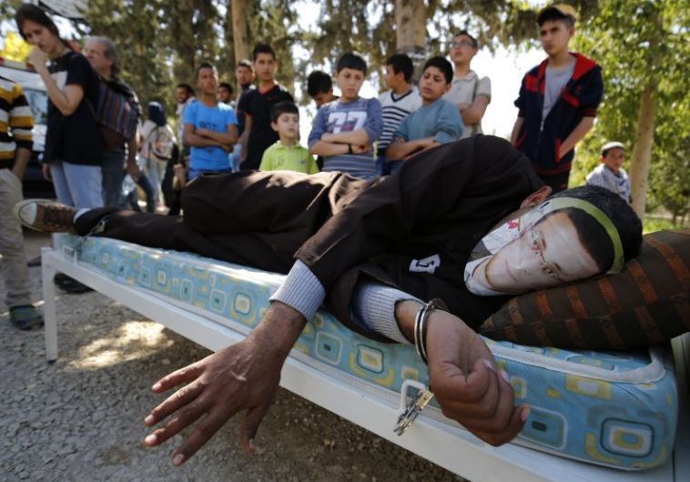 A Palestinian man in Ramallah lies on a bed wears a face covering depicting hunger striking Palestinian journalist Mohammed al-Qiq