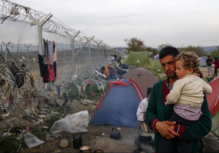 A man with a child looks at the border fence at a makeshift camp for migrants and refugees at the Greek-Macedonian border