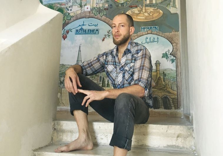 Hillel Efflal sits in front of his mural at the Hostel in Ramallah