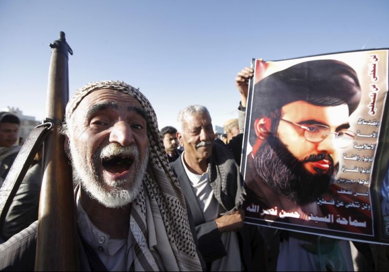 A Houthi militant shouts slogans as he stands next a poster of Hezbollah leader Hassan Nasrallah during a rally against US support to Saudi-led air strikes in Sanaa