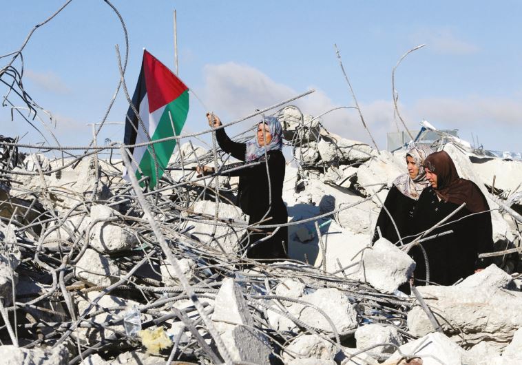 The mother of Palestinian assailant Murad Adais stands with a flag in the rubble of the family’s home in Yatta after it was demolished by the IDF