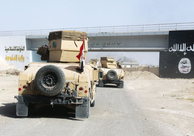 Iraqi military vehicles pass by the flag of Islamic State militants in Falluja, Iraq