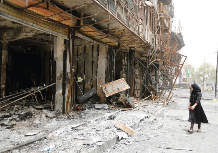 A WOMAN walks past the remains of a building after an attack in Baghdad killed 200 people on Sunday.