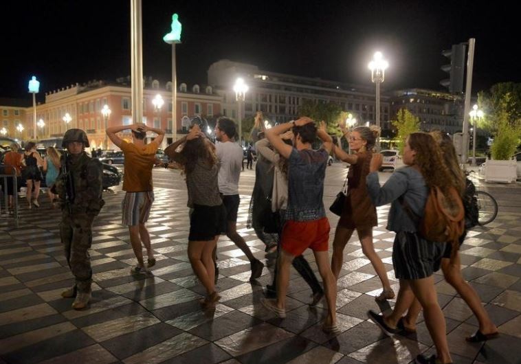 People cross the street with their hands on thier heads as a French soldier secures the area July 15, 2016 after at least 60 people were killed along the Promenade des Anglais in Nice, France, when a truck ran into a crowd celebrating the Bastille Day national holiday July 14. 