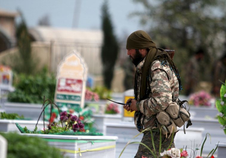 A Kurdish People's Protection Units (YPG) fighter walks near graves of fellow fighters during a visit to a YPG graveyard in Qamishli, Syria