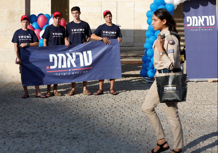 An Israeli soldier walks past members of the US Republican party's election campaign team in Israel, who are holding a banner in support of Republican US presidential nominee Donald Trump, during a campaign aimed at potential American voters living in Israel, near a mall in Modi'in, Israel.