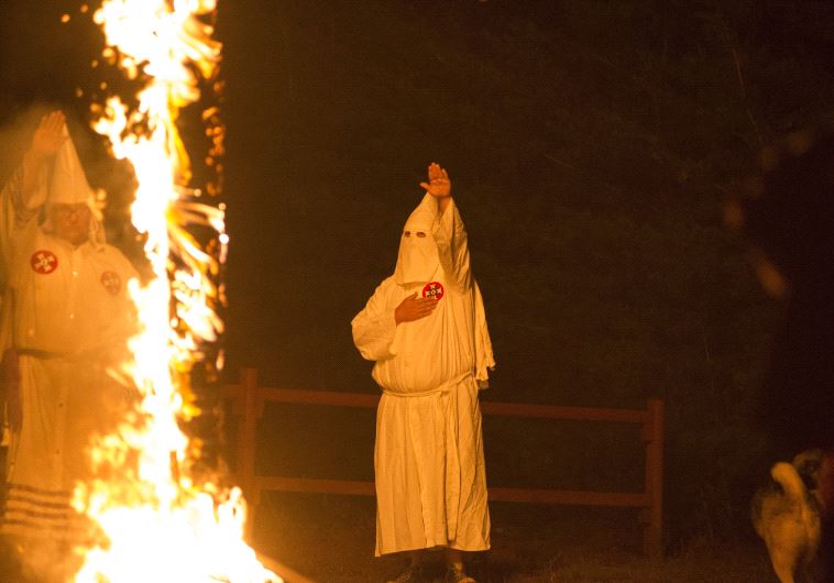A member of the Ku Klux Klan salutes a lit cross during a cross lighting ceremony.