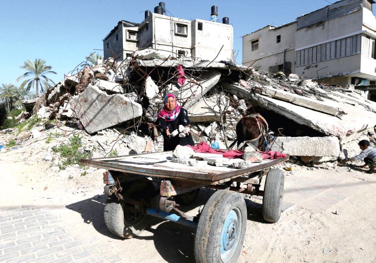 A Palestinian woman collects bricks from a house destroyed during the 2014 Gaza war