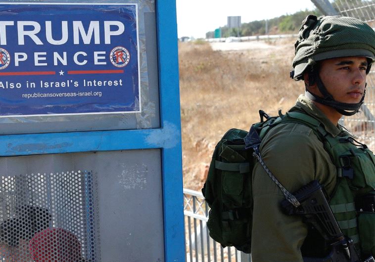 A soldier stands next to a bus stop with a pro-Trump poster near the West Bank Jewish settlement of Ariel